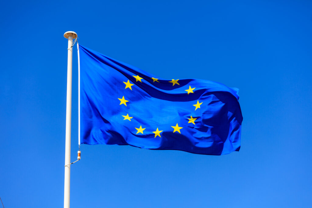 EU flag. European Union flag on a flagpole waving on a bright blue sky background