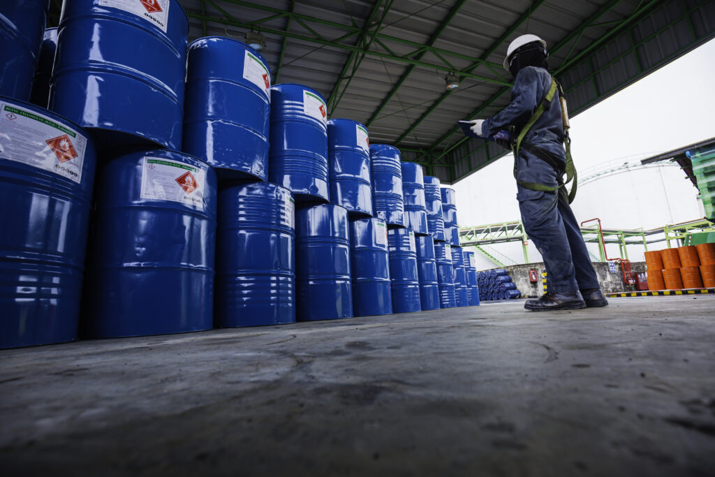 Worker inspecting stacked blue barrels for chemical  distribution 
